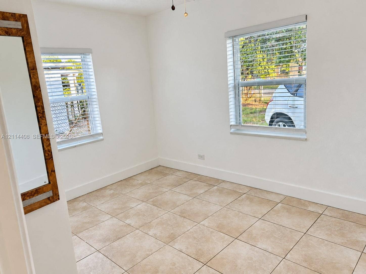 Neutral-toned tile flooring, dual windows with white horizontal blinds, and a built-in wall-mounted mirror with a decorative wood-finish frame
