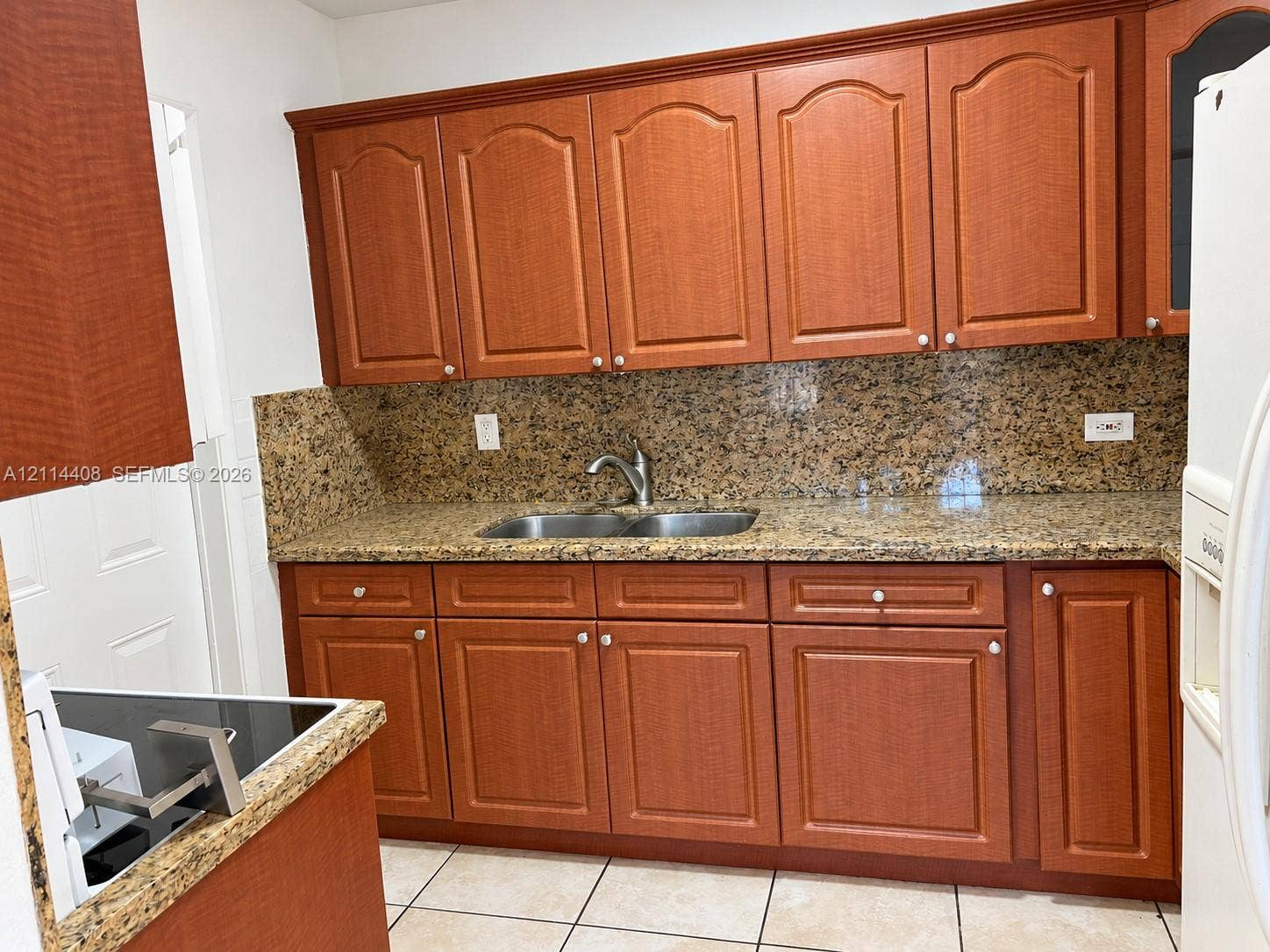 Kitchen featuring stained wood cabinetry, stone countertops, stone backsplash, double-basin stainless steel sink, and ceramic tile flooring