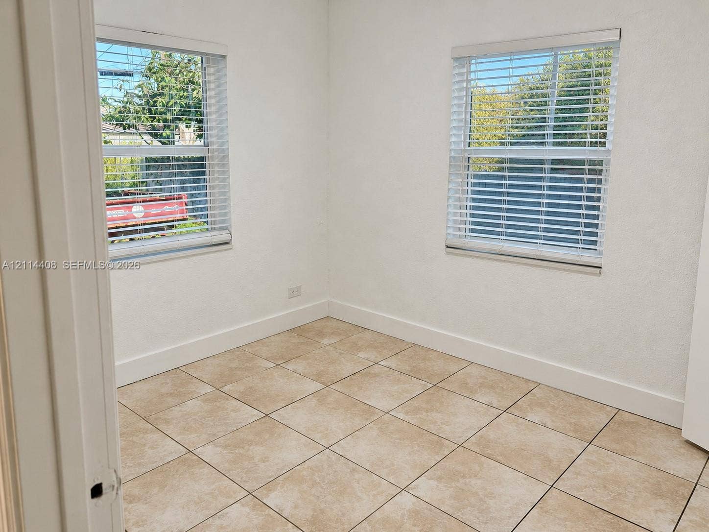 Room featuring neutral-toned tile flooring, two windows with horizontal blinds, and smooth-finish white walls