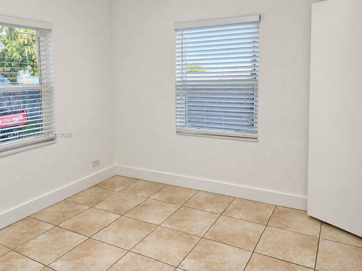 Neutral interior featuring light-colored tile flooring, smooth wall finishes, and two windows equipped with horizontal blinds