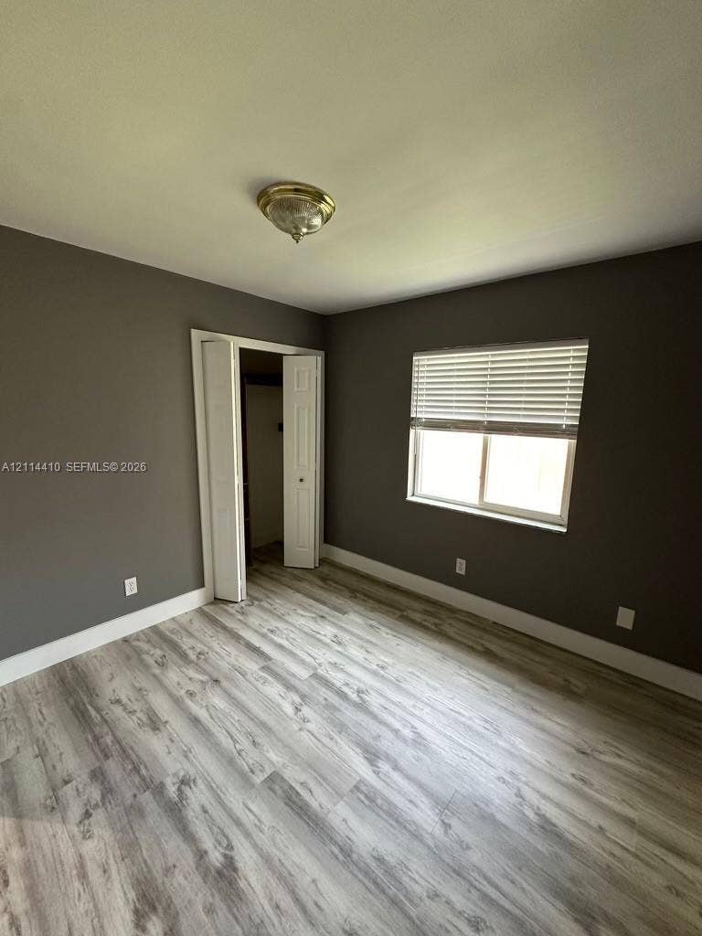 Room featuring wood-finish flooring, neutral-toned walls, a double-panel closet door, and a horizontal window with fitted blinds