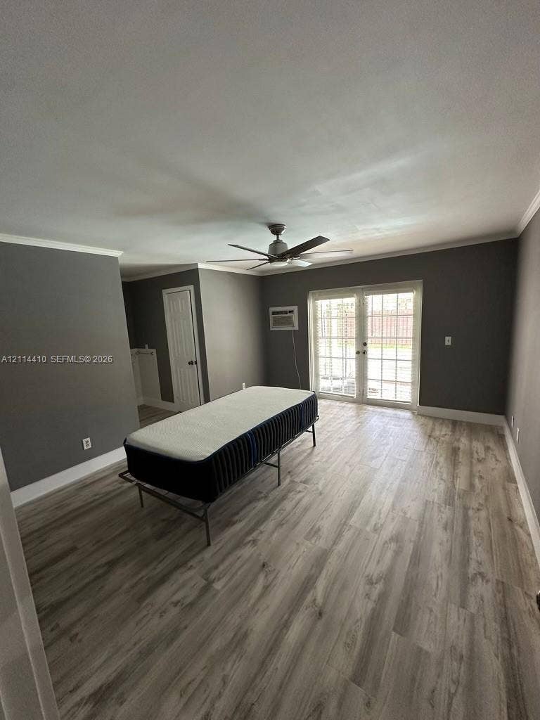 Wood-finish flooring, neutral wall tones, multi-light French doors, ceiling fan, and wall-mounted air conditioning unit