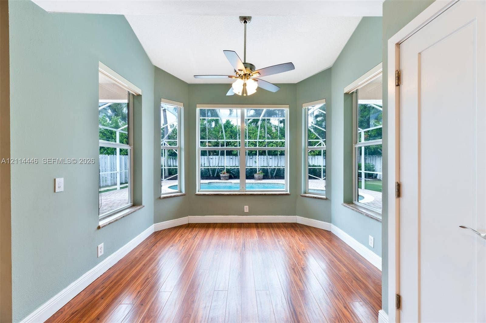 Bay window with multiple glass panes, vaulted ceiling, wood-finish flooring, and a ceiling-mounted light fixture with fan
