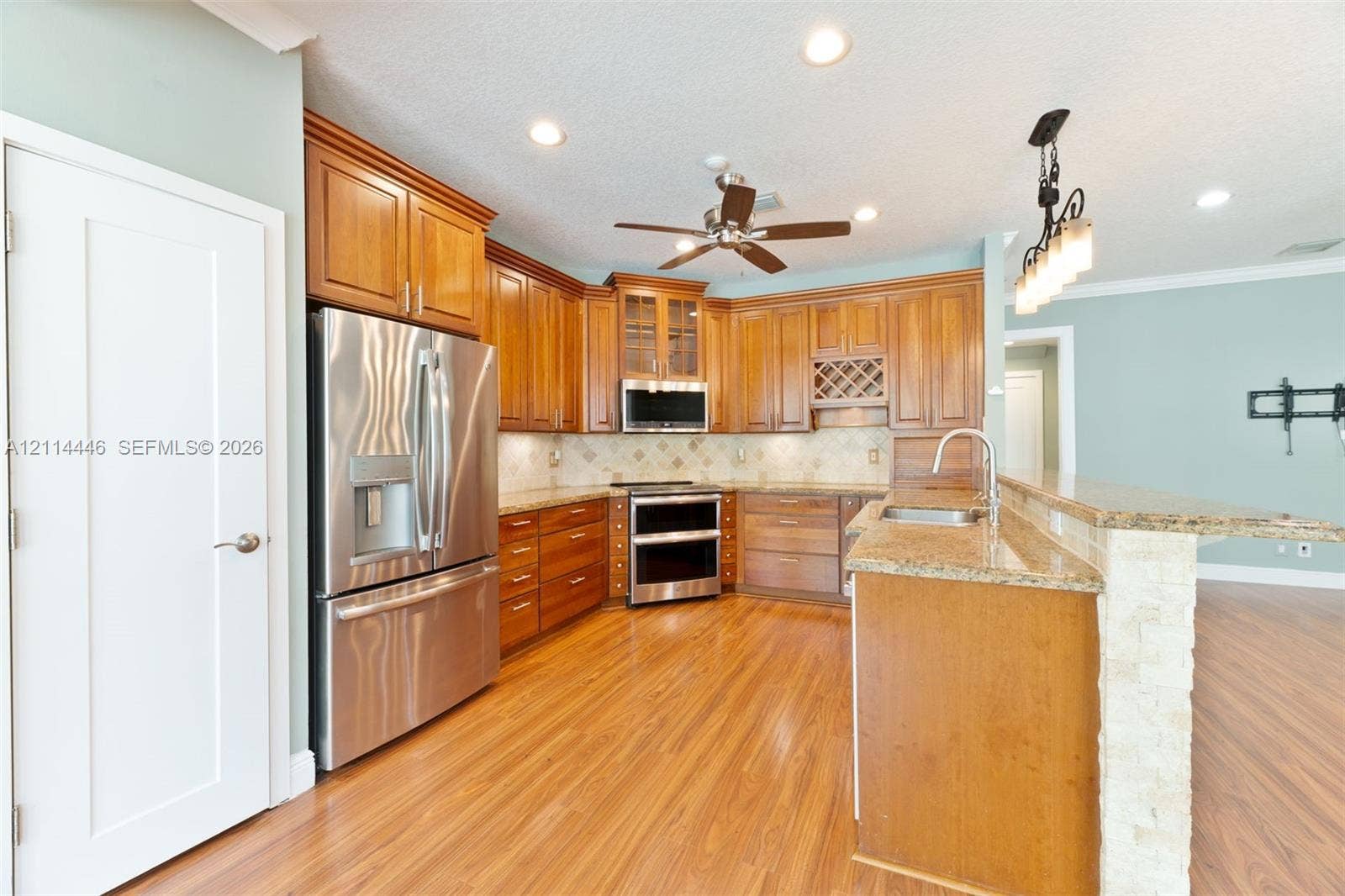Kitchen featuring stained wood cabinetry, stone countertops, stainless steel appliances, a built-in wine rack, and wood-finish flooring