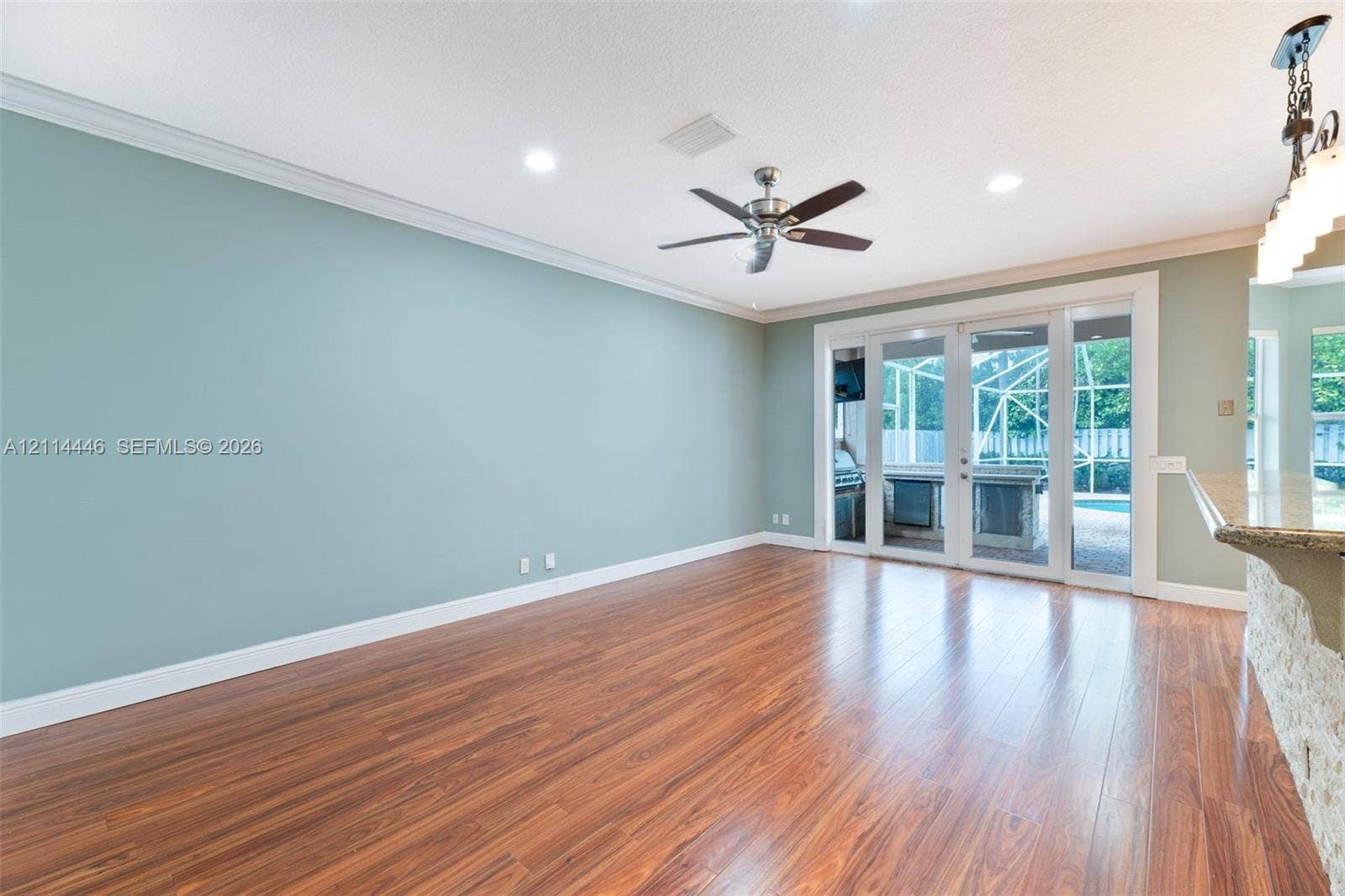 Wood-finish flooring, crown molding, recessed lighting, brushed metal ceiling fan, and multi-panel glass door leading to an enclosed outdoor area