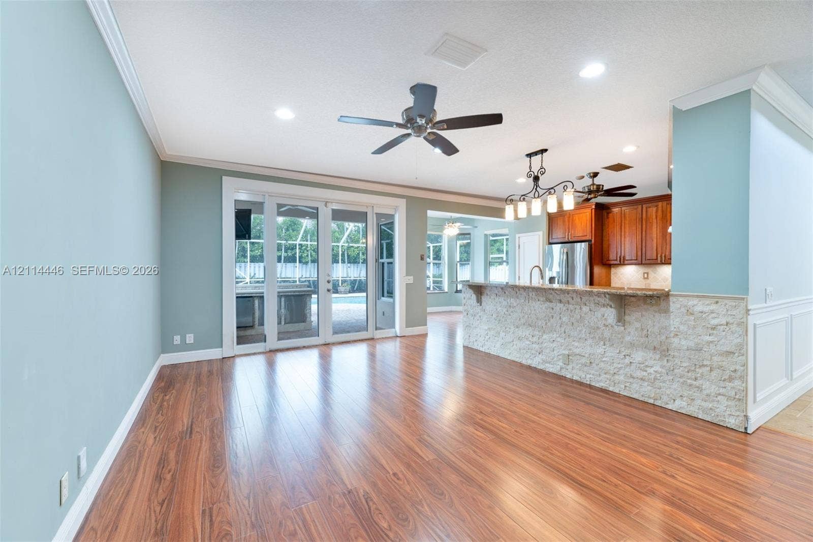 Open-concept area featuring wood-finish flooring, a tiered breakfast bar with stone-veneer facing, recessed lighting, ceiling fans, and multi-panel glass doors