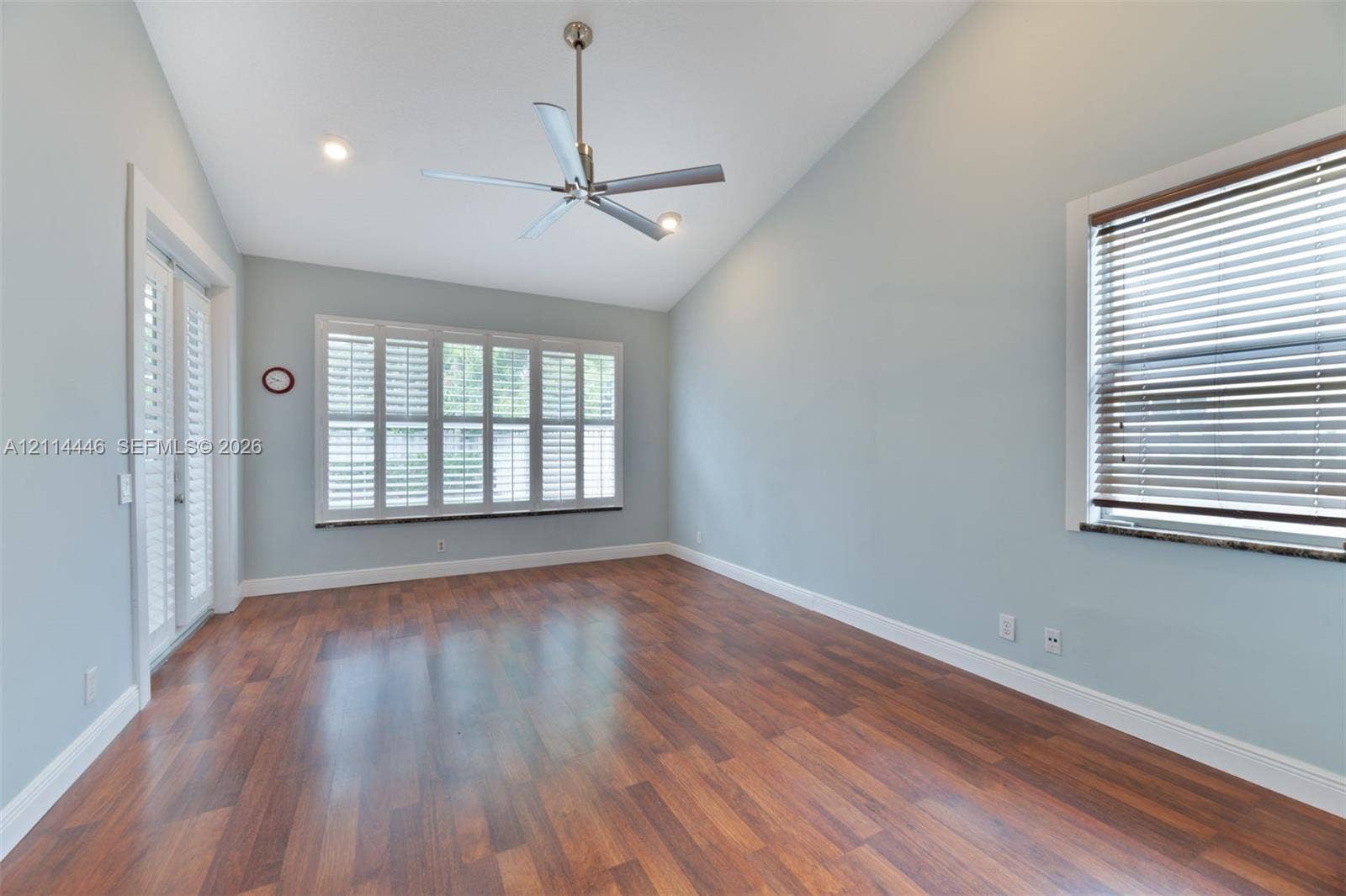 Vaulted ceiling, wood-finish flooring, multi-pane window with plantation shutters, recessed lighting, and dual glass-pane doors