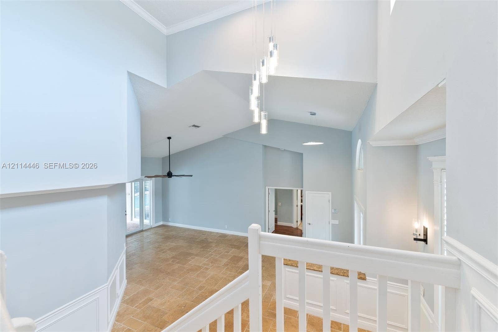 Vaulted ceilings with multi-pendant lighting, tile flooring, white wainscoting, and a white baluster railing