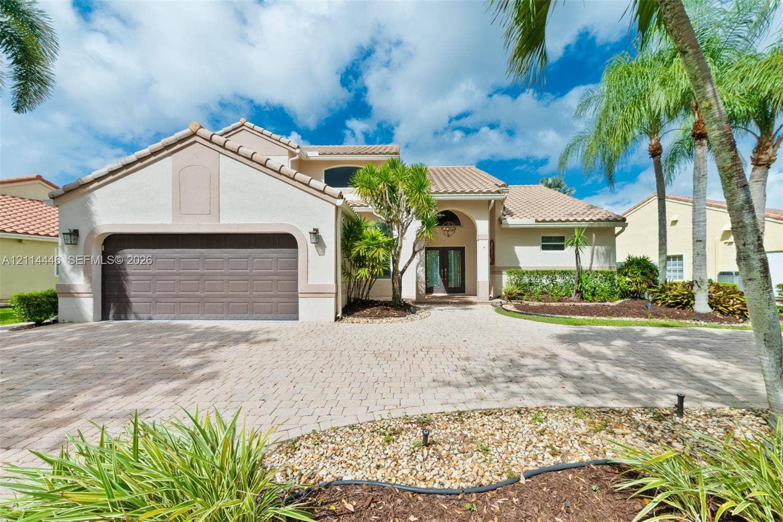Stucco exterior featuring a tile roof, multi-car garage, arched entryway, and paver driveway