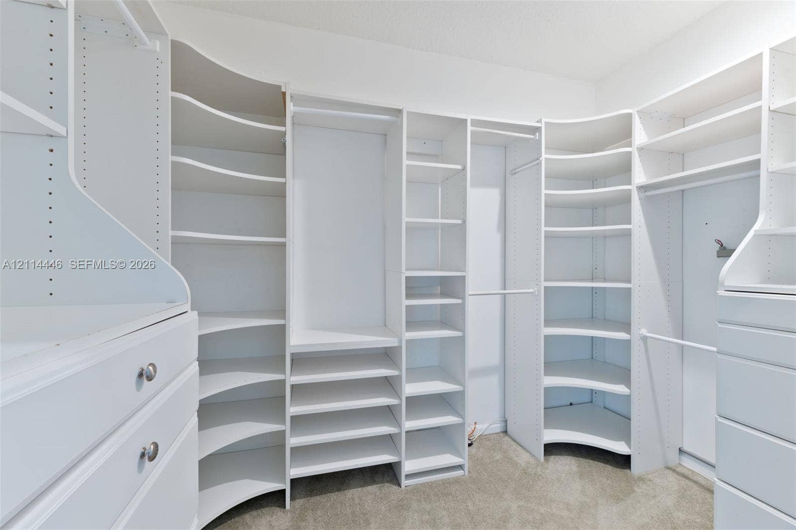 Walk-in closet featuring white built-in shelving, adjustable storage cubbies, curved corner shelves, and integrated drawers with metallic hardware
