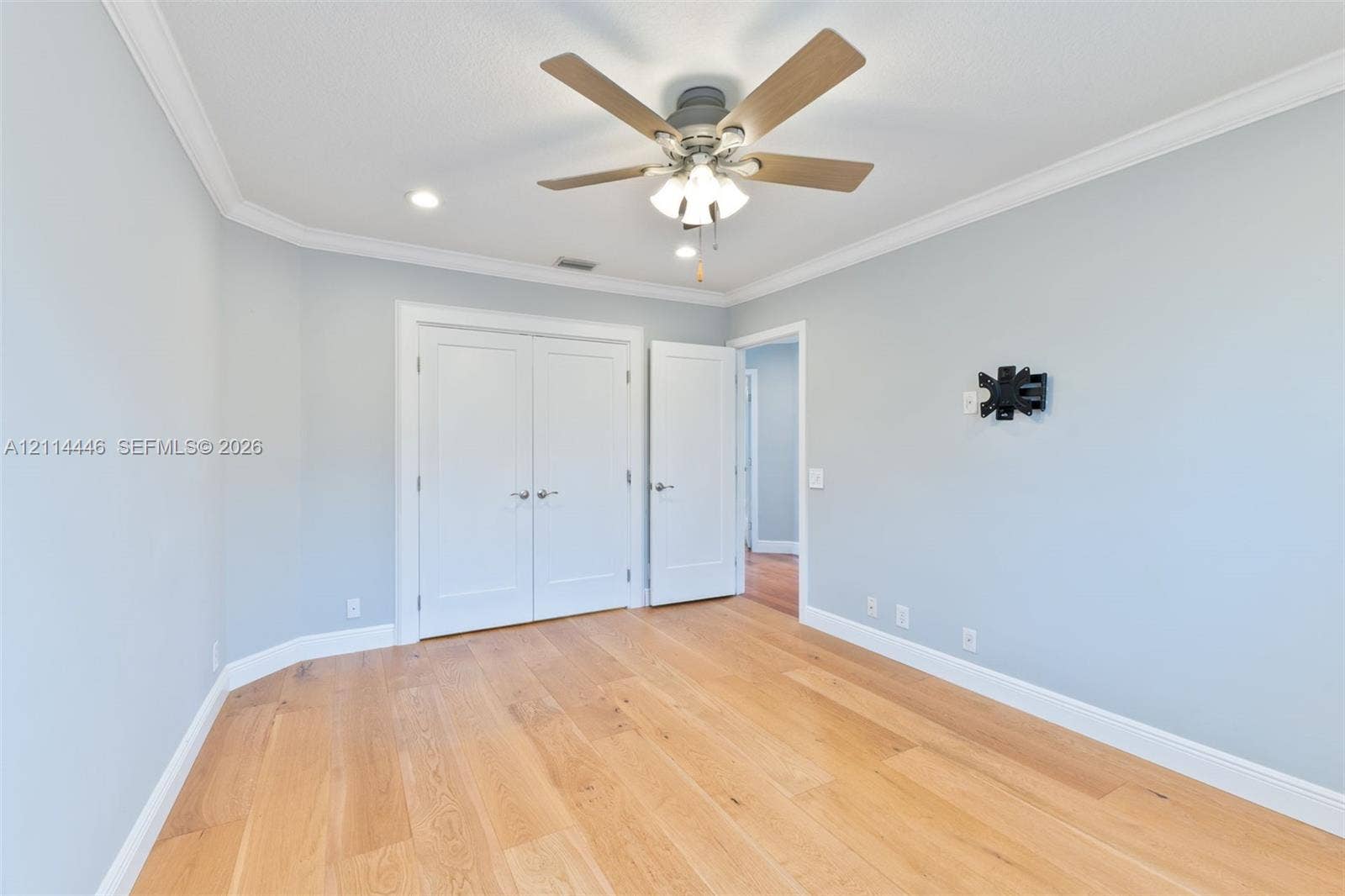 Light-filled room featuring wood-finish flooring, a multi-blade ceiling fan with integrated lighting, recessed ceiling lights, and double-door closet cabinetry