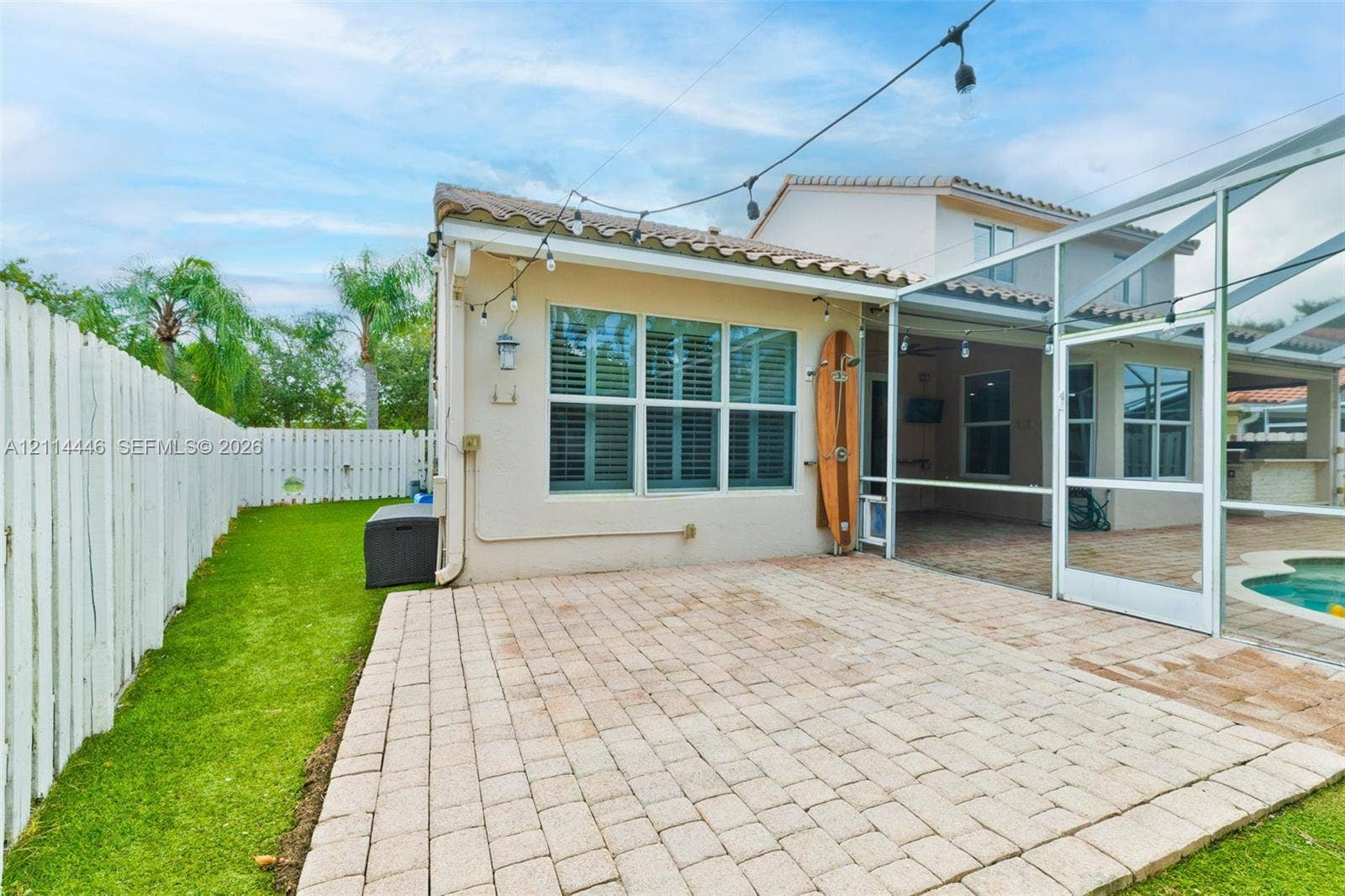 Paver patio featuring a screened-in enclosure, concrete tile roofing, and a white privacy fence