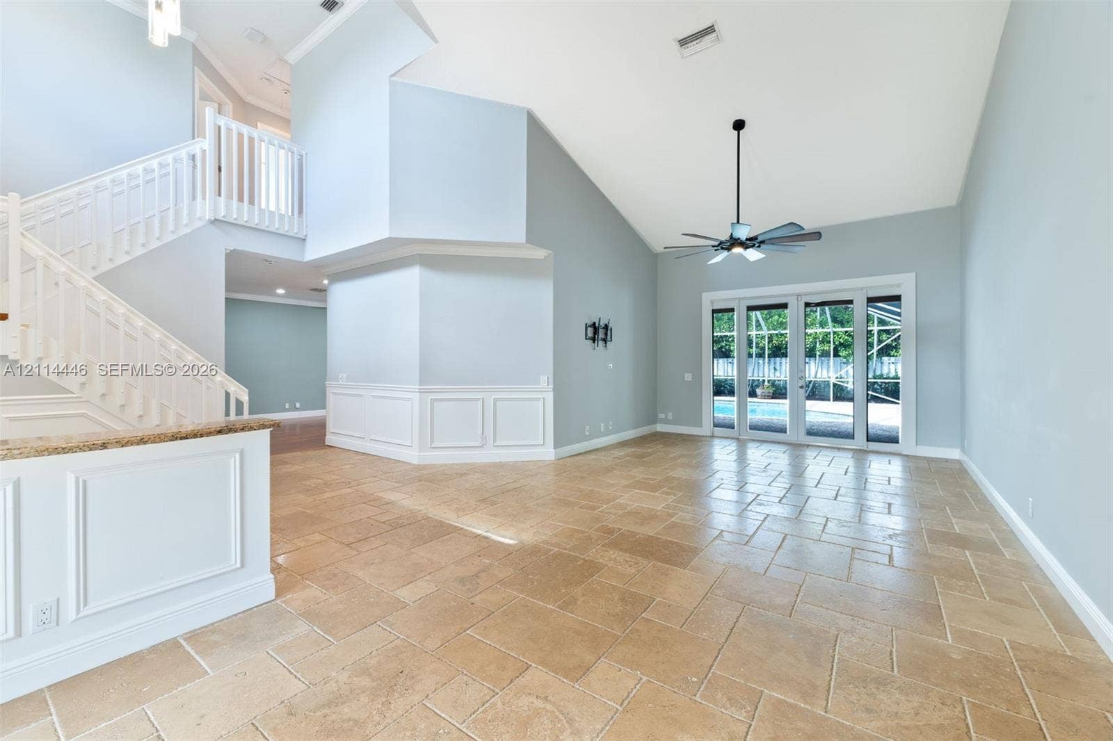 Open-concept interior featuring vaulted ceilings, tile flooring in a running bond pattern, a staircase with white balusters, wainscoting wall detailing, and multi-panel glass doors