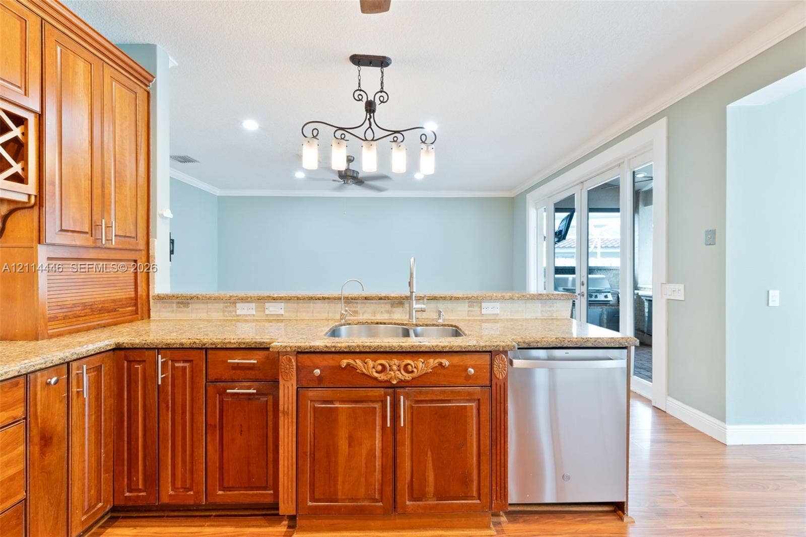 Kitchen featuring medium-toned wood cabinetry, stone countertops, stainless steel dishwasher, decorative carved wood detail, and a multi-light chandelier