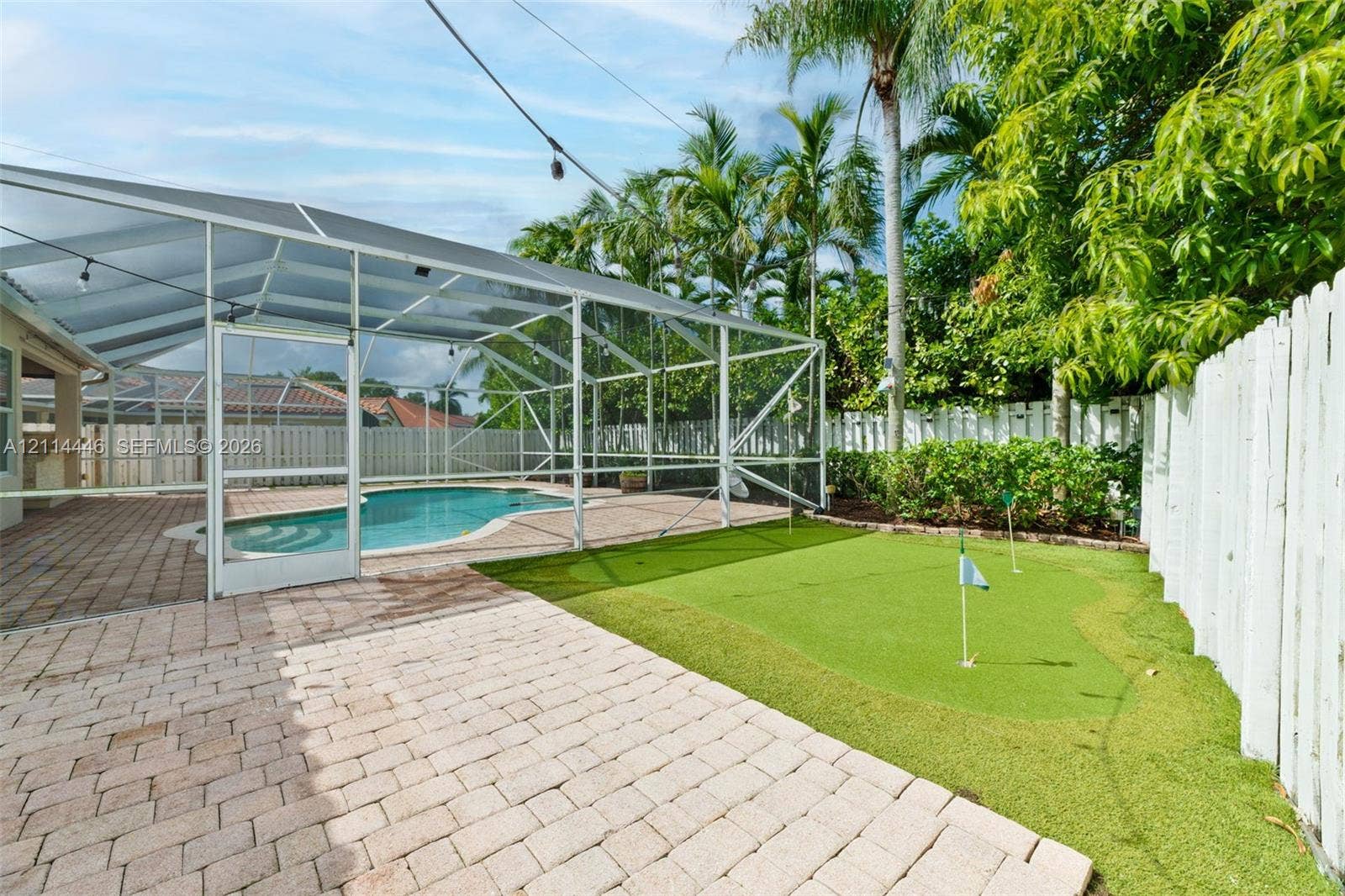 Screen-enclosed swimming pool, paver patio, integrated putting green, and perimeter wood fencing