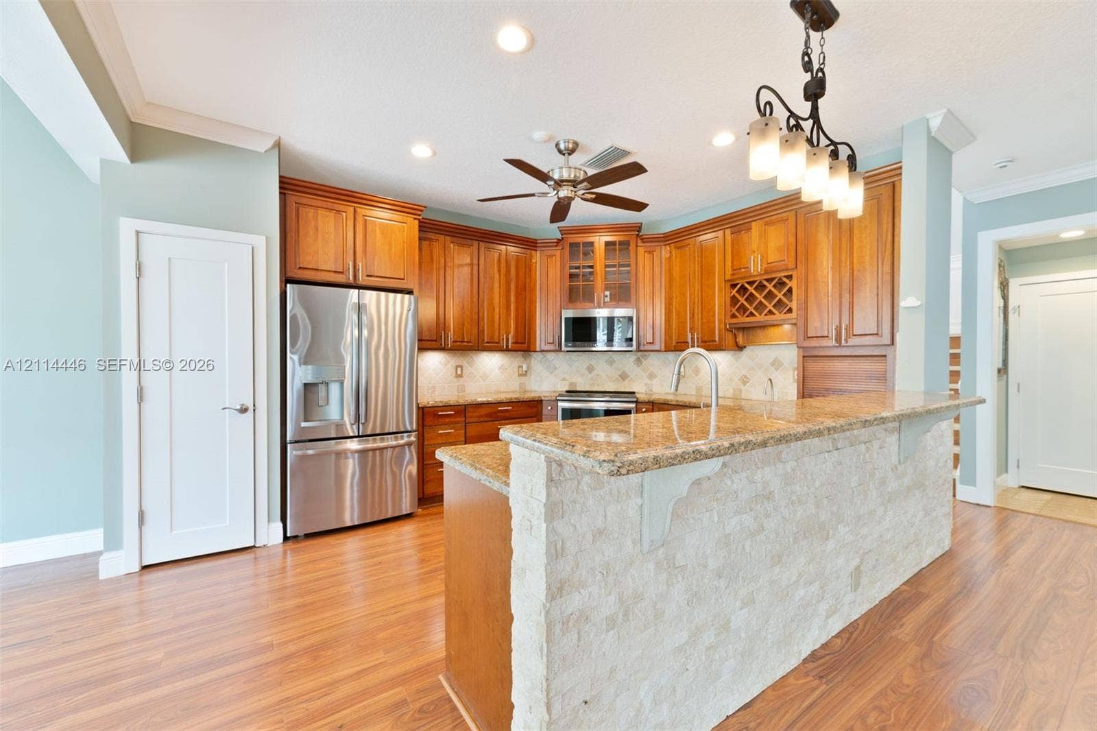 Kitchen featuring stained wood cabinetry, stone-clad breakfast bar, natural stone-finish countertops, stainless steel appliances, and multi-light pendant fixture