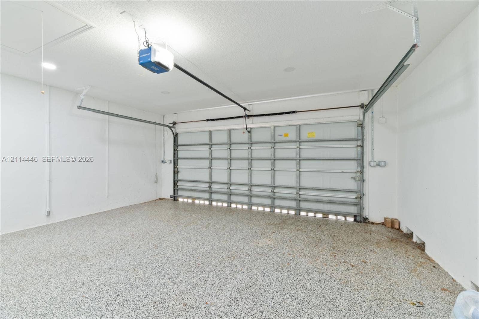 Two-car garage featuring epoxy-coated flooring, white interior walls, and an automated overhead door system