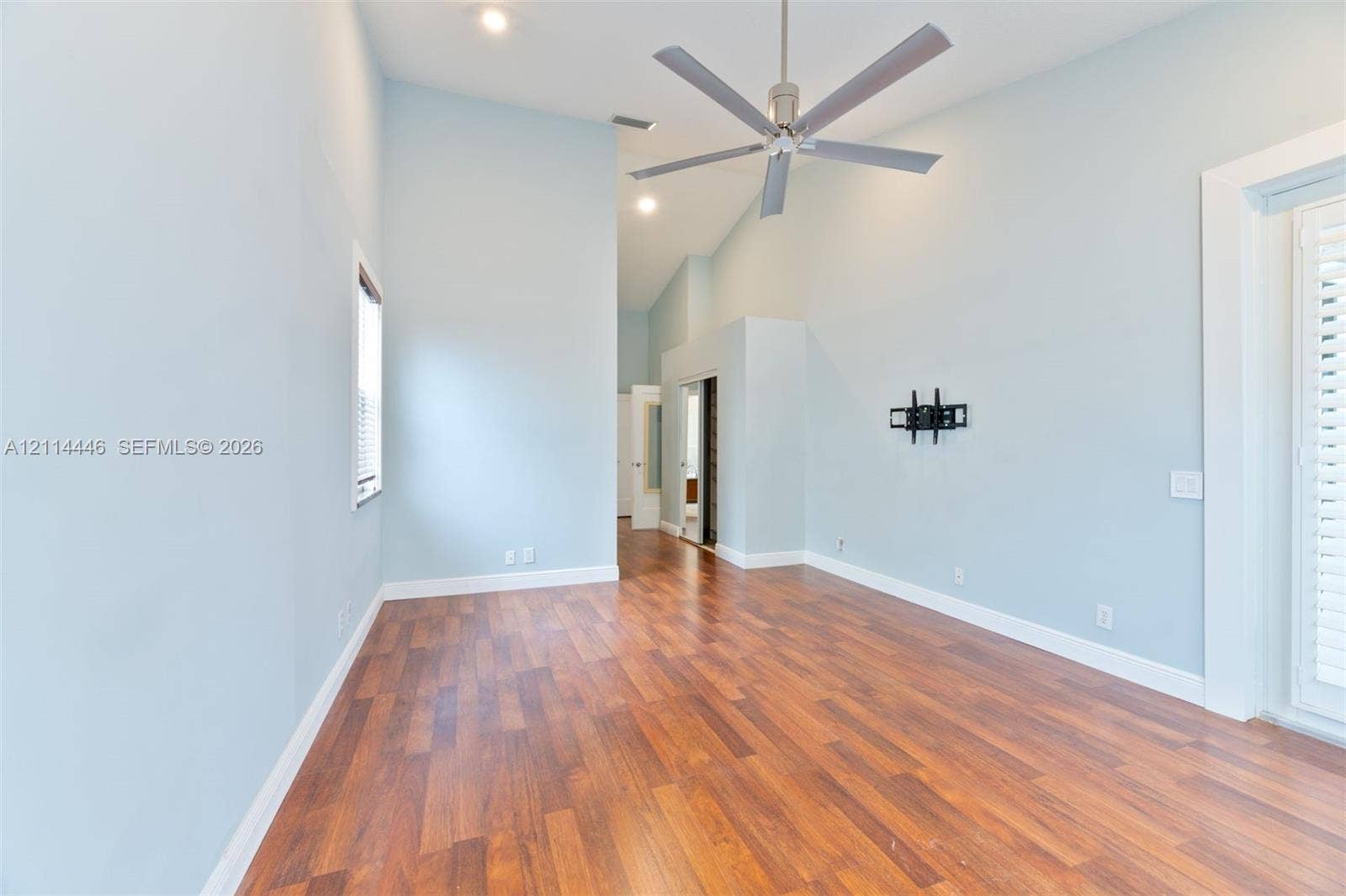 Vaulted ceilings featuring recessed lighting, a brushed-metal ceiling fan, wood-finish flooring, and a glass-paneled exterior door with shutters