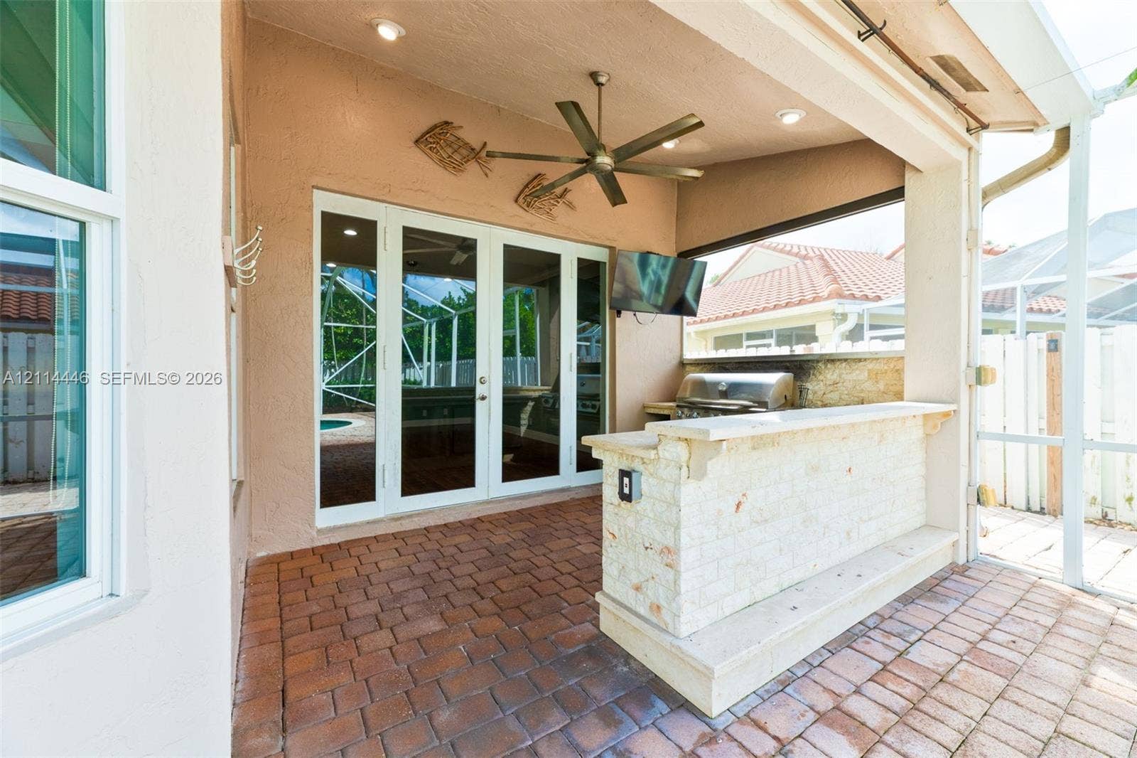 Screened-in patio featuring brick paver flooring, stone-veneer outdoor bar with countertop, built-in stainless steel grill, and ceiling fan