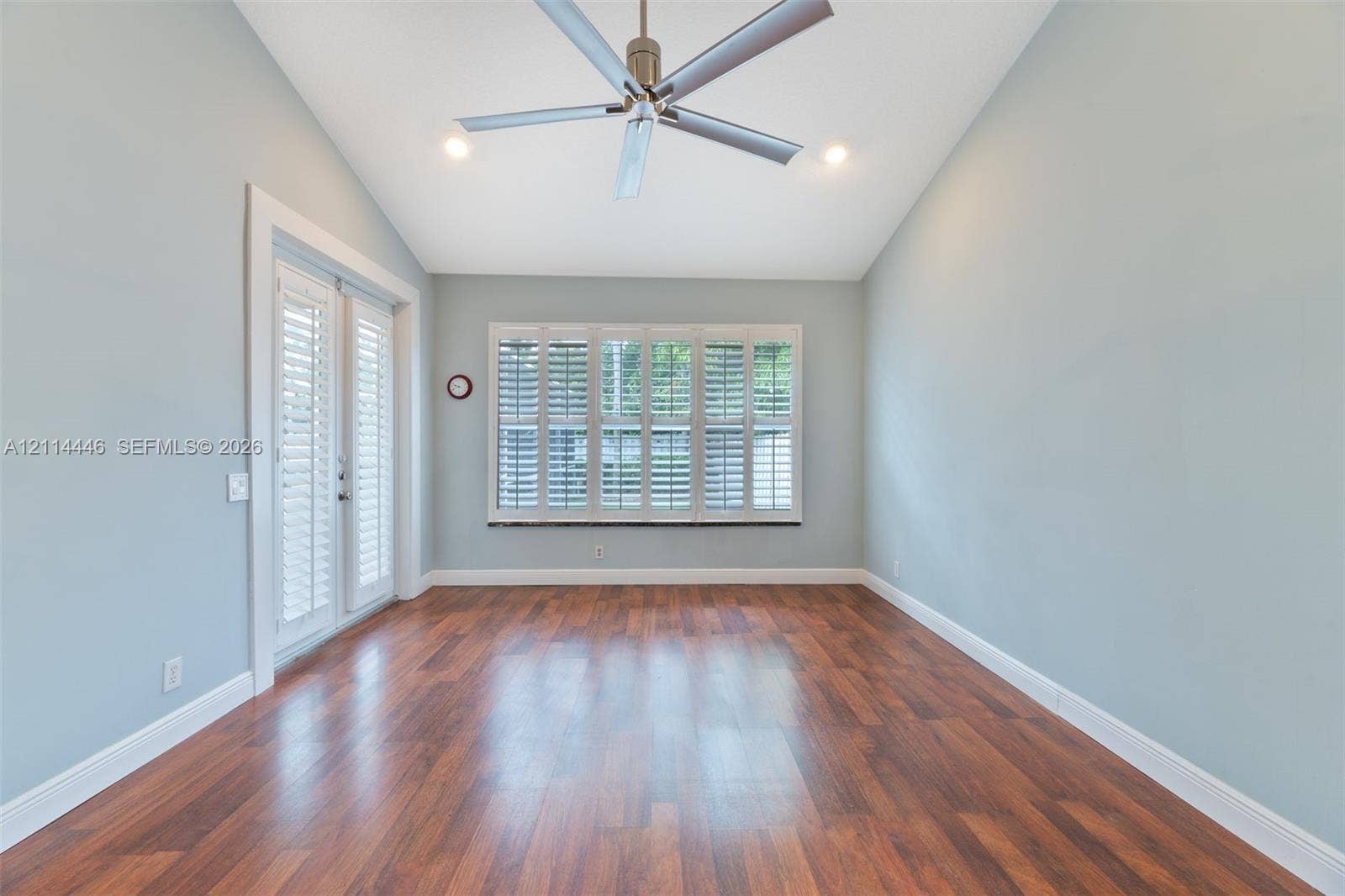 Vaulted ceiling room featuring wood-finish flooring, recessed lighting, a modern ceiling fan, plantation shutters, and glass-paneled double doors