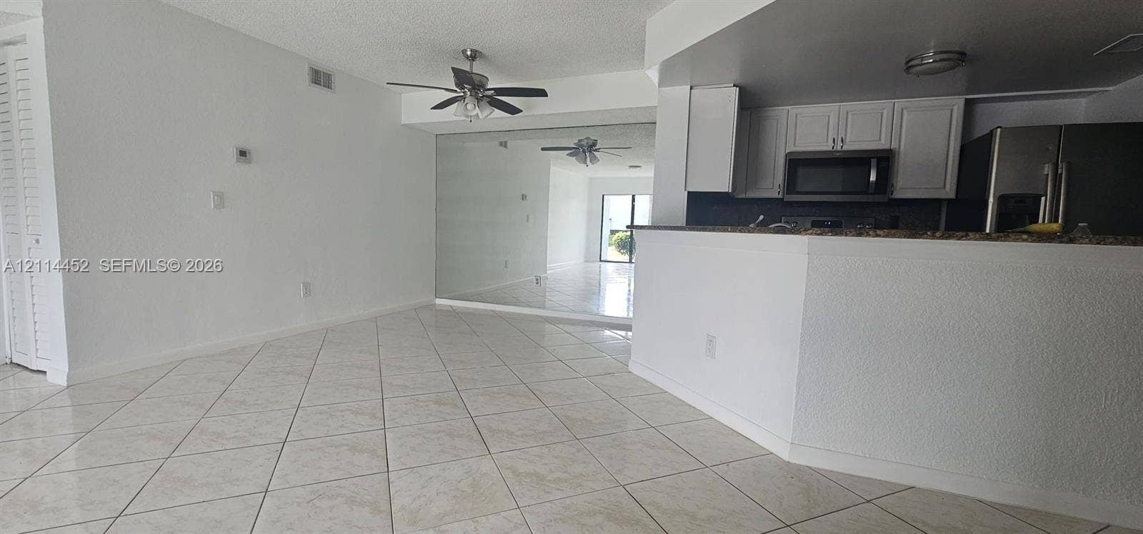 9044 W Atlantic Boulevard, #314, Coral Springs, Coral Springs, FL 33071 Open-concept interior featuring diagonal tile flooring, white cabinetry, dark stone-finish countertops, built-in ceiling fans, and a full-height wall mirror