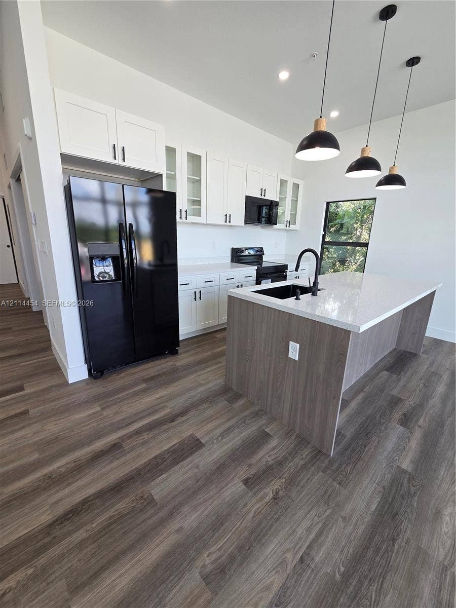 401 Pembroke Road, #203, Hallandale Beach, Hallandale Beach, FL 33009 Kitchen featuring white cabinetry, wood-finish flooring, a central island with a quartz countertop, black hardware, and three pendant lights