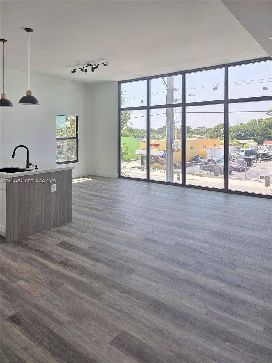 401 Pembroke Road, #203, Hallandale Beach, Hallandale Beach, FL 33009 Open-concept interior featuring floor-to-ceiling windows, wood-finish flooring, a kitchen island with a quartz countertop, and black matte pendant lighting
