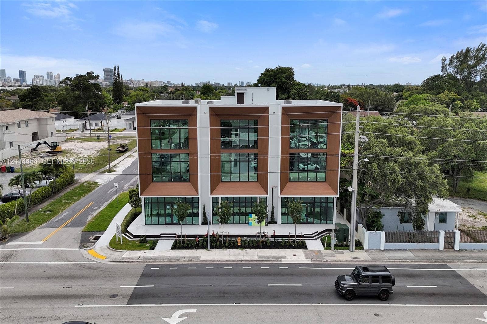 401 Pembroke Road, #203, Hallandale Beach, Hallandale Beach, FL 33009 Modern three-story commercial facade featuring expansive floor-to-ceiling glass windows, recessed metallic-finish paneling, and a landscaped concrete exterior plaza