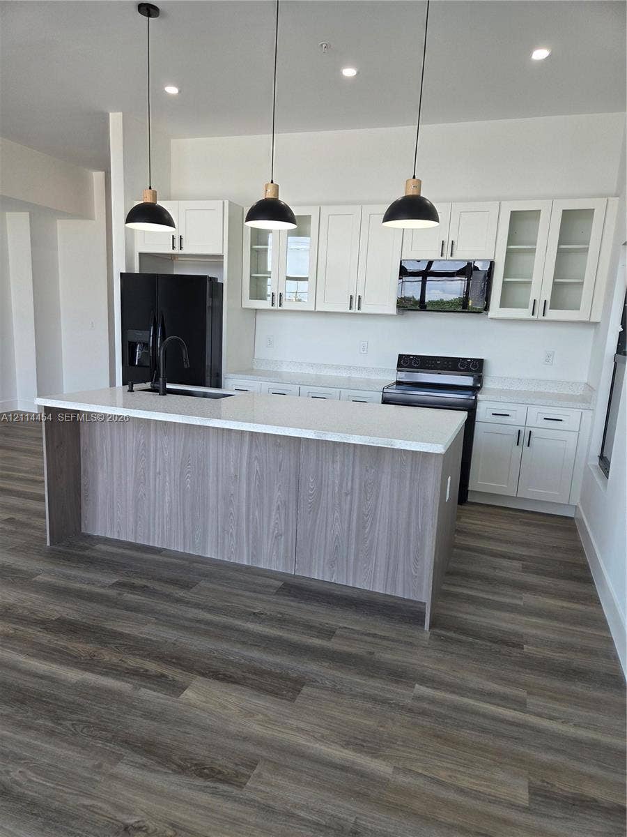 401 Pembroke Road, #203, Hallandale Beach, Hallandale Beach, FL 33009 Kitchen featuring white Shaker-style cabinetry, a central island with wood-finish paneling, quartz countertops, black pendant lighting, and wood-finish flooring