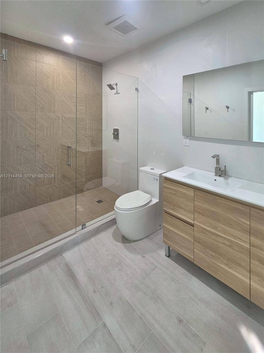 401 Pembroke Road, #203, Hallandale Beach, Hallandale Beach, FL 33009 Walk-in shower with textured tile surround, frameless glass enclosure, wood-finish vanity, integrated rectangular sink, and neutral-tone large-format floor tile