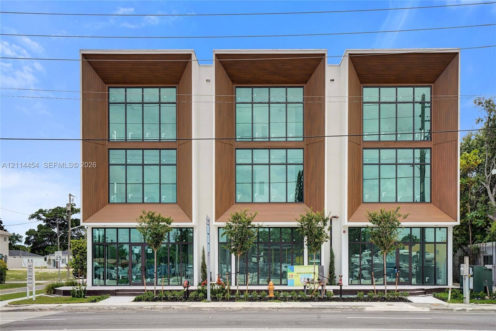 401 Pembroke Road, #203, Hallandale Beach, Hallandale Beach, FL 33009 Contemporary three-story structure featuring a smooth stucco exterior, wood-finish paneling, floor-to-ceiling glass windows, and metal-framed storefront entries