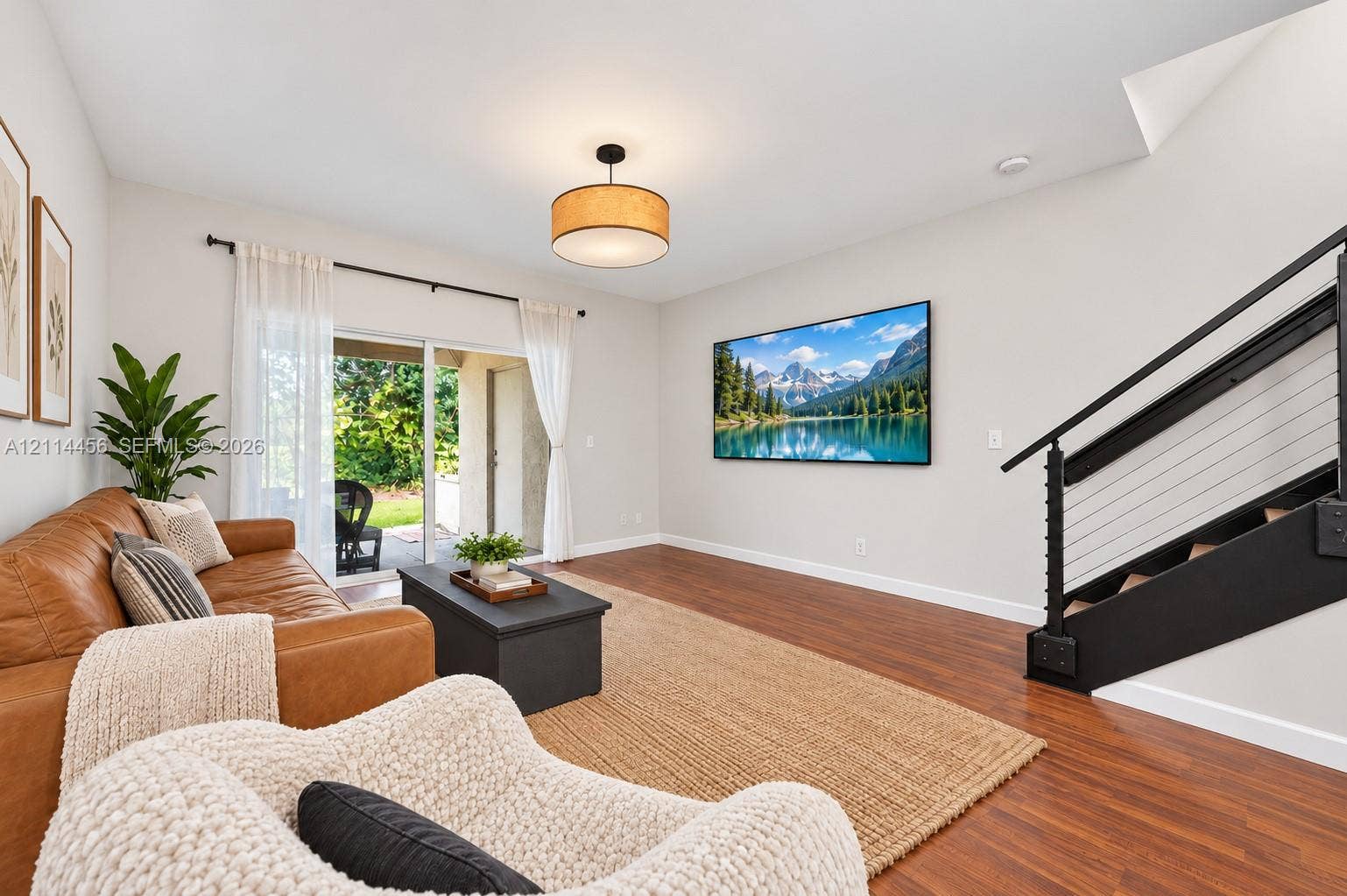 Living area featuring wood-finish flooring, a drum pendant light fixture, and a staircase with a black metal railing and horizontal cable infill