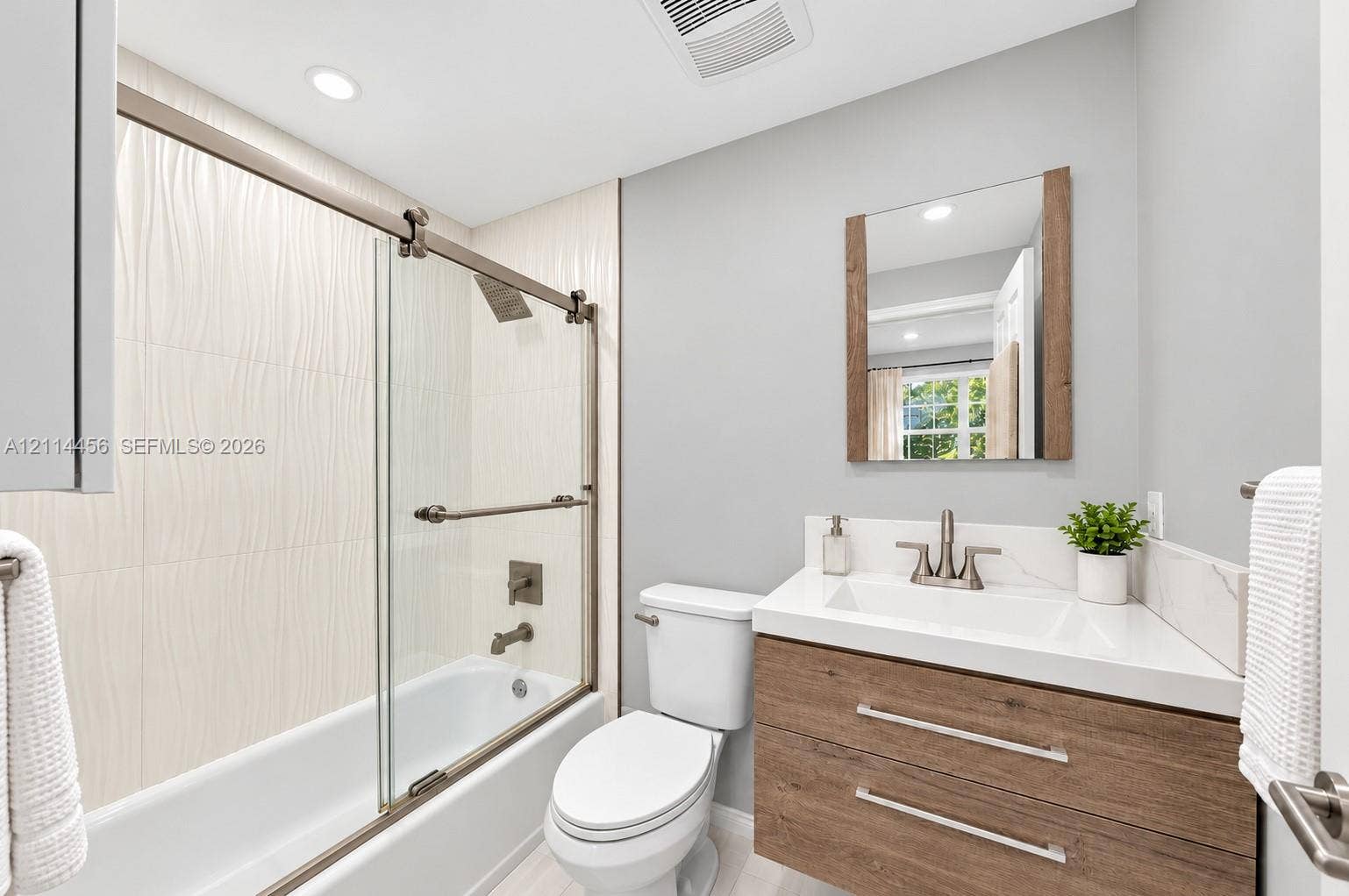 Floating wood-finish vanity with a white countertop, integrated sink, sliding glass shower enclosure, and textured tile wall surround