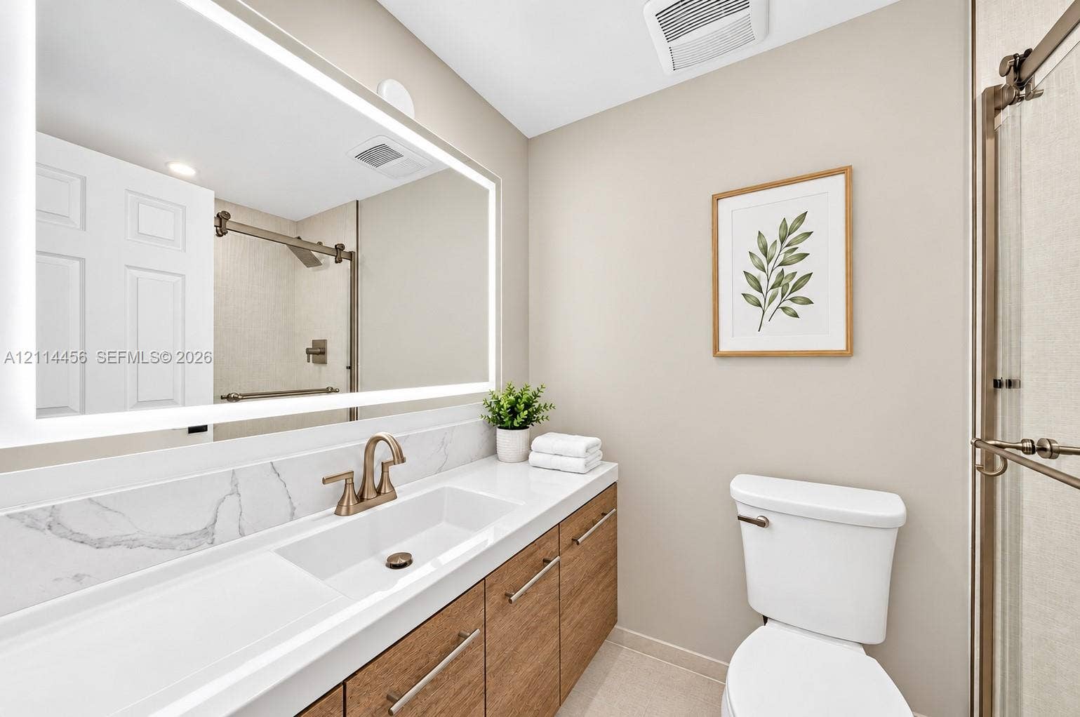 Bathroom featuring a wood-finish vanity with a stone-top integrated sink, LED-backlit mirror, brushed-finish faucet hardware, and a glass-enclosed shower