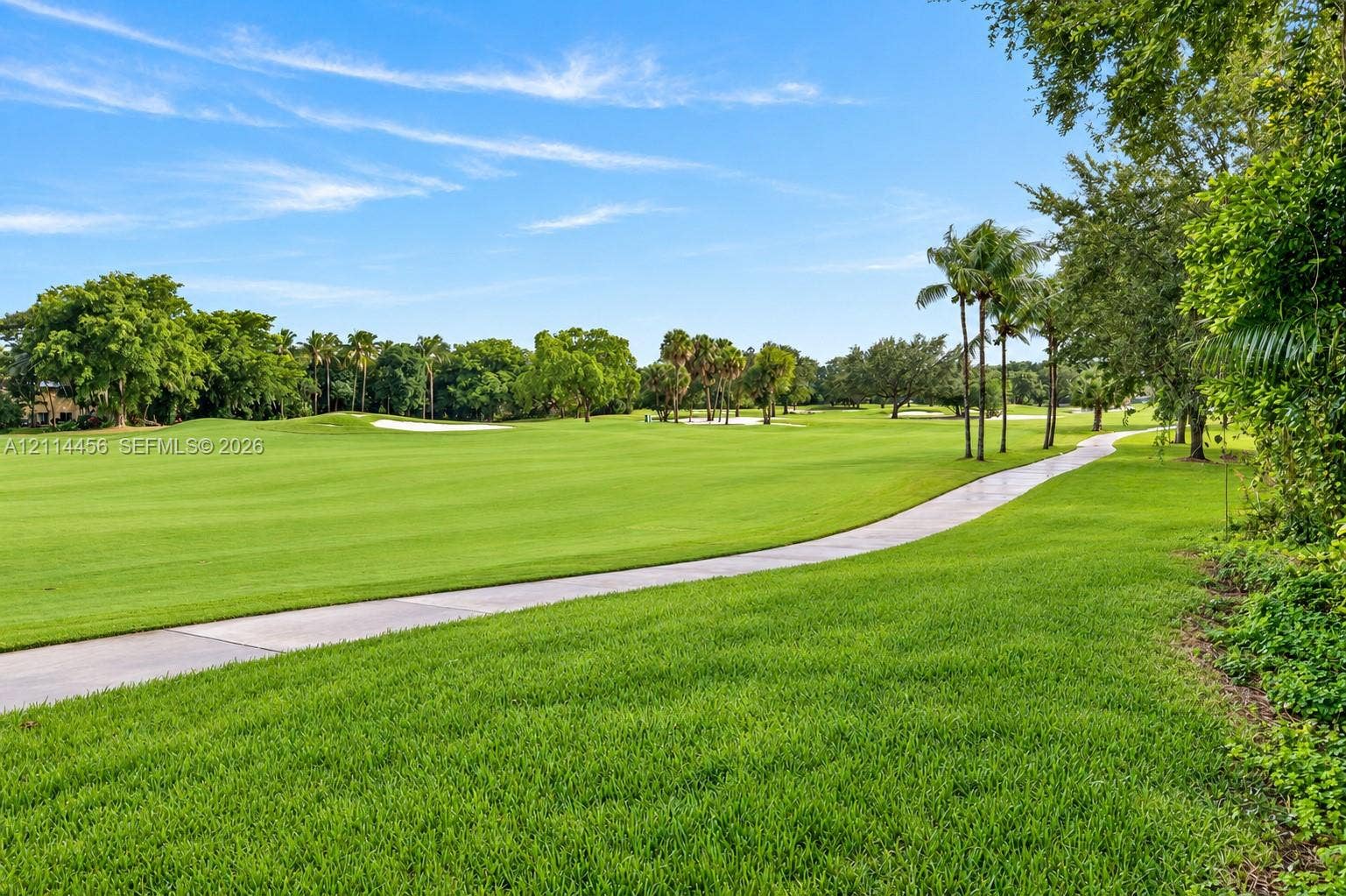 Expansive manicured lawn, concrete pathway, mature trees, and sand bunkers