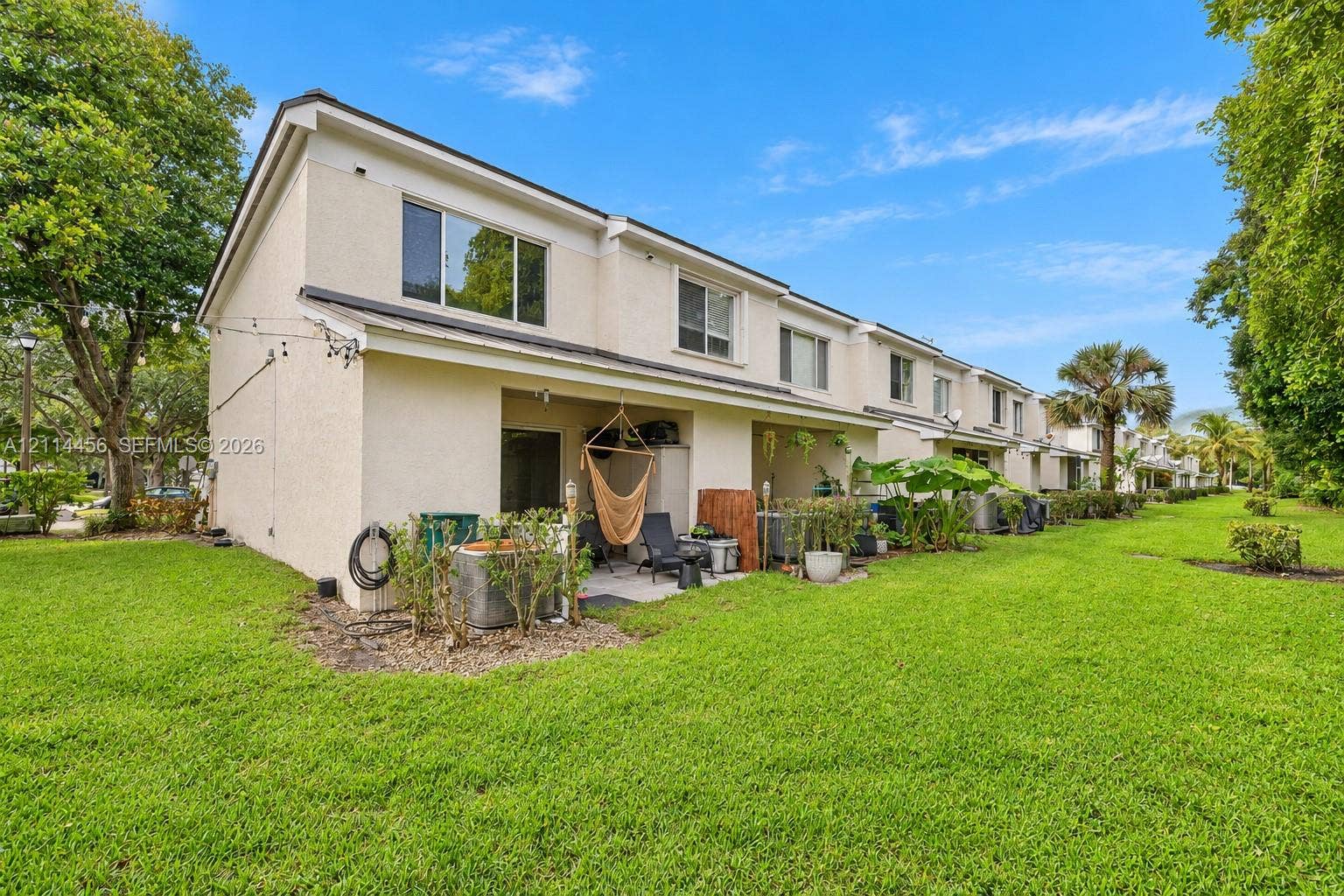 Two-story structure featuring a stucco exterior, multi-pane windows, and a covered ground-level patio space situated on an expansive manicured lawn