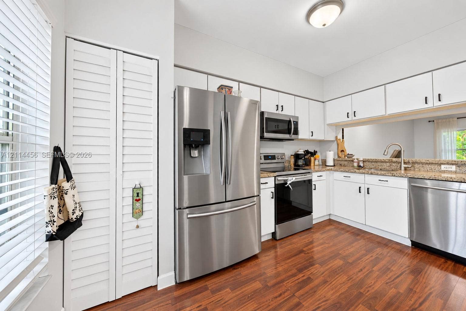 Kitchen featuring white cabinetry, stone-finish countertops, stainless steel appliances, wood-finish flooring, and louvered-style closet doors