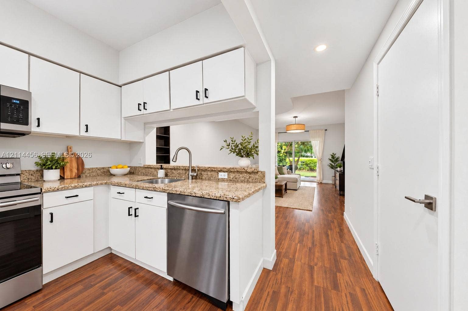Kitchen featuring white cabinetry with dark hardware, stone countertops, stainless steel appliances, and wood-finish flooring