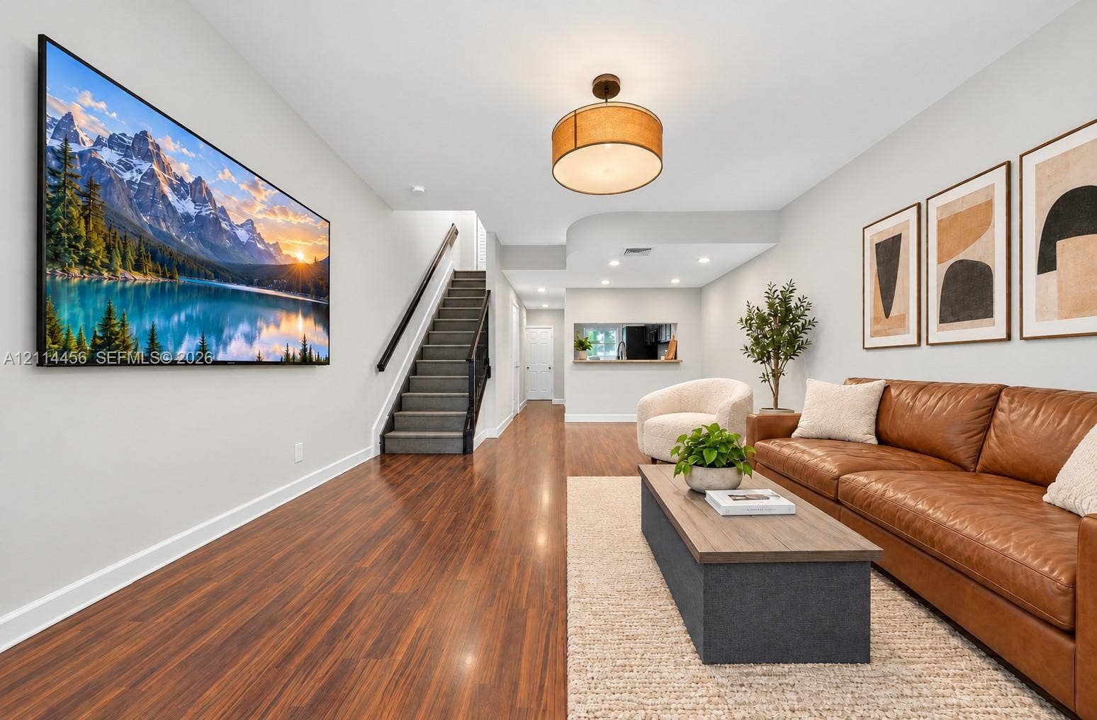 Wood-finish flooring, staircase with a dark-finished handrail, drum-style ceiling light fixture, recessed lighting, and a wall cutout featuring a pass-through counter