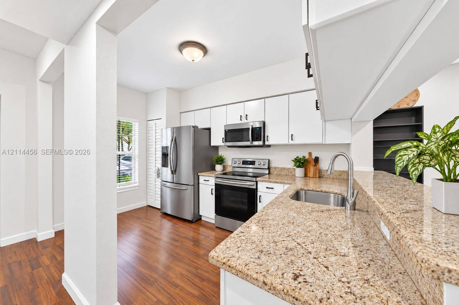 Kitchen featuring white cabinetry, stone countertops, stainless steel appliances, a double-basin sink, and wood-finish flooring