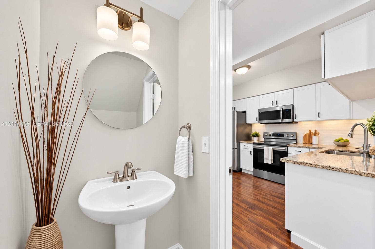 Powder room featuring a white pedestal sink, circular mirror, and brushed-nickel wall-mounted light fixture