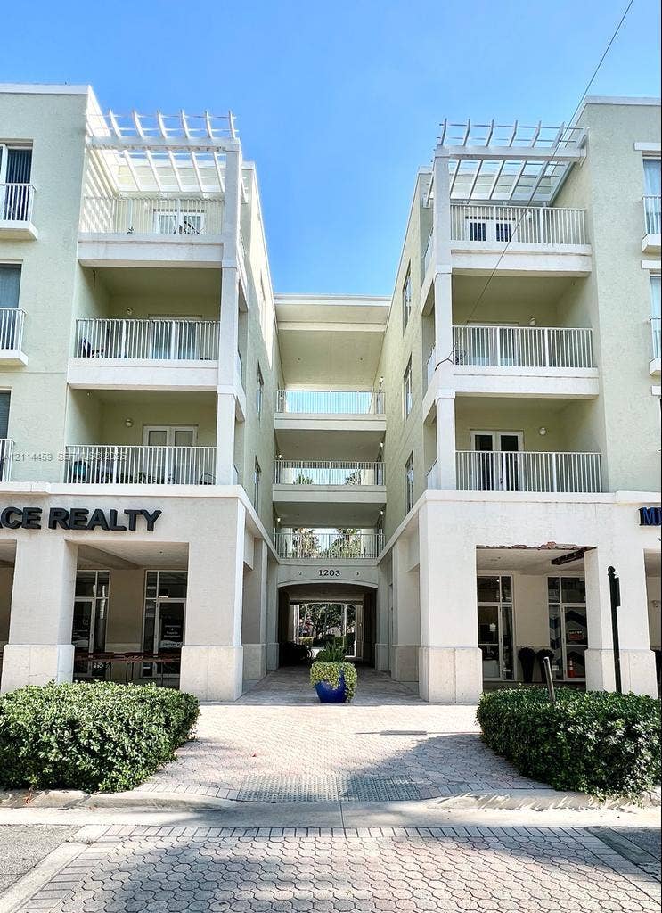 1203 Town Center Drive, #207, Jupiter, Jupiter, FL 33458 Multi-story mixed-use building featuring stucco exterior, private balconies with metal railings, top-level pergolas, and a paved pedestrian thoroughfare