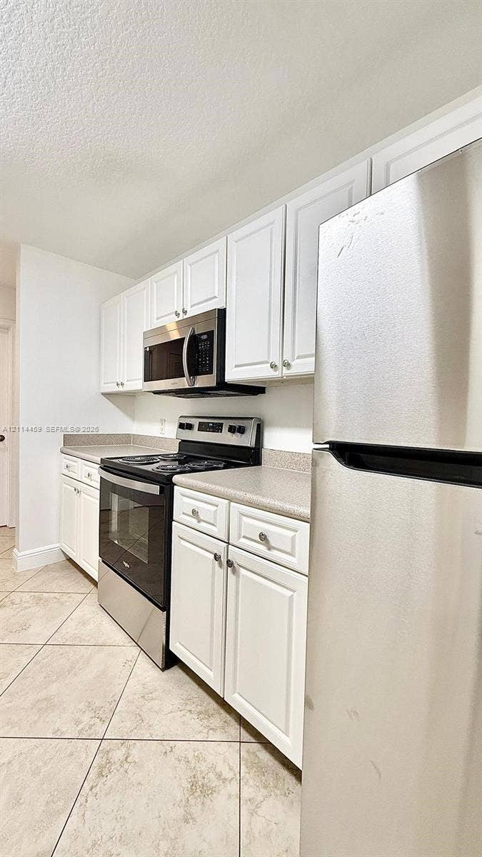 1203 Town Center Drive, #207, Jupiter, Jupiter, FL 33458 Kitchen featuring white cabinetry, solid-surface countertops, stainless steel appliances, and tile flooring