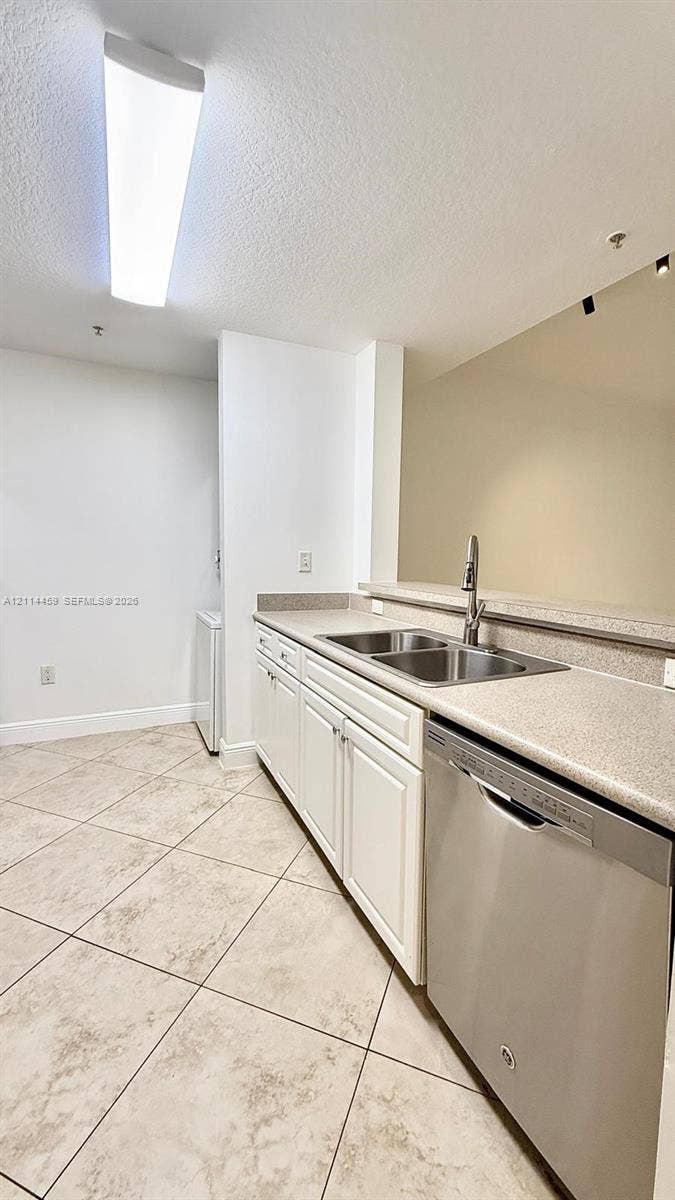 1203 Town Center Drive, #207, Jupiter, Jupiter, FL 33458 Kitchen featuring solid-surface countertops, dual-basin stainless steel sink with a high-arc faucet, stainless steel dishwasher, white cabinetry, and tile flooring