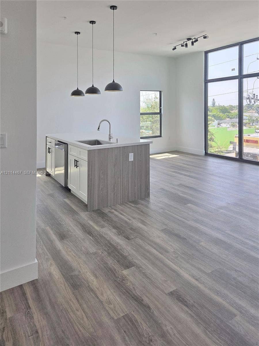 Kitchen island featuring two-tone cabinetry and stone countertops, complemented by wood-finish flooring, floor-to-ceiling windows, and matte black pendant lighting