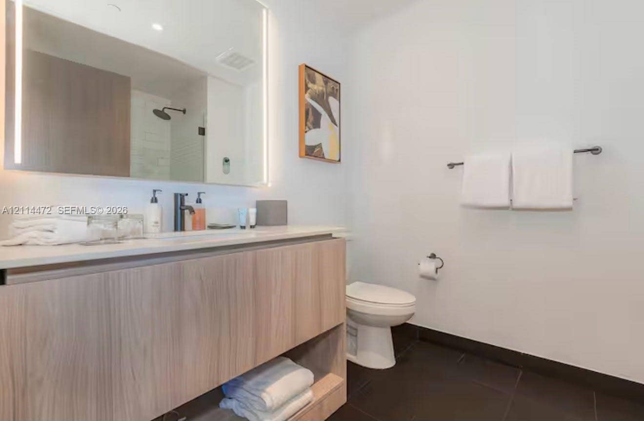 398 NE 5th Street, #4001, Miami, FL 33132 Floating vanity with wood-finish cabinetry and light-toned countertop, large rectangular mirror with integrated LED lighting, matte black fixtures, and dark-toned floor tile