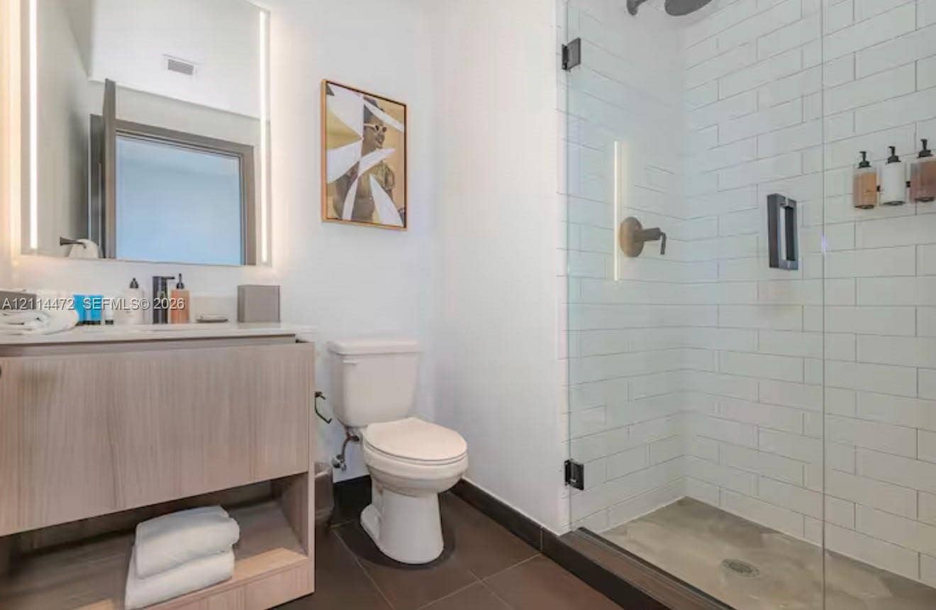 398 NE 5th Street, #4001, Miami, FL 33132 Wood-finish floating vanity with an integrated countertop, illuminated wall-mounted mirror, walk-in shower with white subway tile surround, and large-format tile flooring