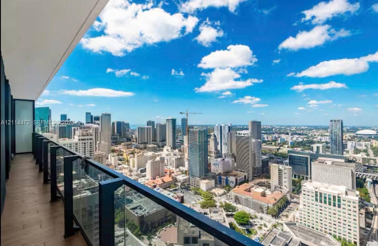 398 NE 5th Street, #4001, Miami, FL 33132 Covered balcony featuring wood-finish flooring and a glass panel railing with metal supports, overlooking an expansive cityscape