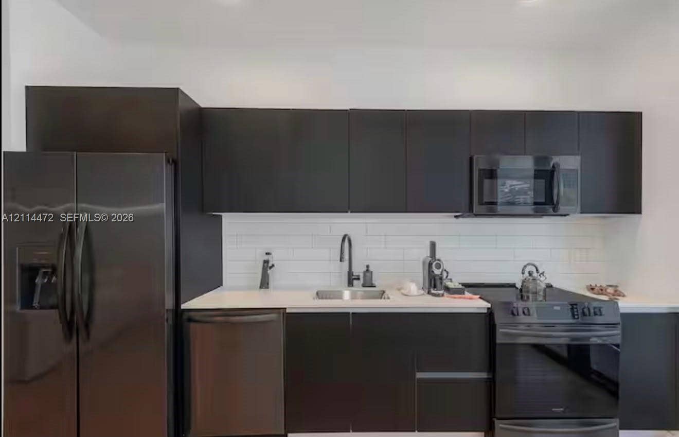 398 NE 5th Street, #4001, Miami, FL 33132 Modern kitchen featuring flat-panel cabinetry, a white subway tile backsplash, light-toned countertops, a stainless steel undermount sink, and matte black hardware