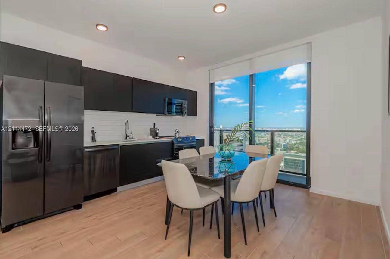 398 NE 5th Street, #4001, Miami, FL 33132 Modern kitchen featuring matte black flat-panel cabinetry, white horizontal tile backsplash, stainless steel appliances, wood-finish flooring, and floor-to-ceiling windows